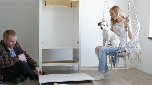 A Man Gathering A Wardrobe, A Woman With A Dog Swinging On A Swing Nearby