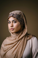 Fototapeta na wymiar Studio portrait of a beautiful, young and attractive Muslim Middle Eastern woman in a brown hijab head scarf and traditional outfit for Eid (Ramadan, Raya). She is elegant and dignified.