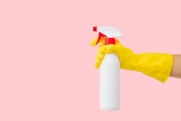Woman hand in yellow rubber protective glove holding white plastic spray bottle on pastel pink...