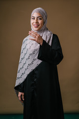 Portrait of a tall, slim and elegant Muslim Middle Eastern woman in a black dress and white hijab head scarf smiling and laughing as she poses for her head shot in a studio.