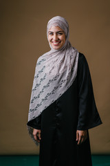 Portrait of a tall, slim and elegant Muslim Middle Eastern woman in a black dress and white hijab head scarf smiling and laughing as she poses for her head shot in a studio. 