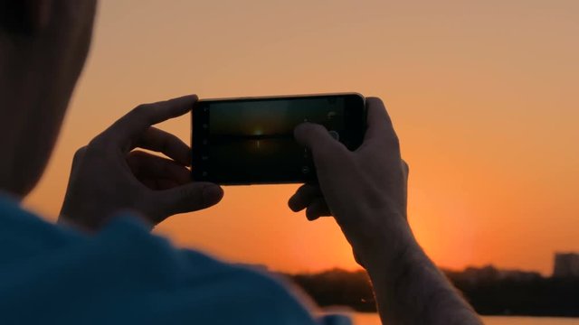 Man taking photo of beautiful sunset with smartphone in city. Sunset light, golden hour. Photography, nature and journey concept. Close up shot of man hands with phone