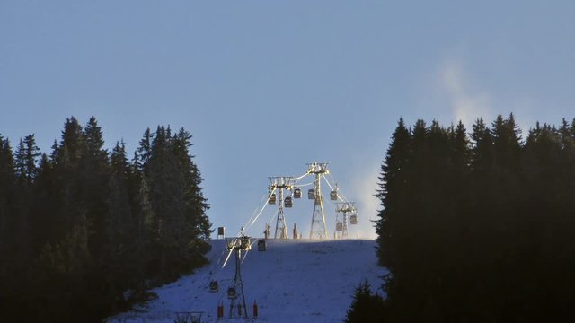 Time lapse of a bubble ski lift passing through a gap in a forest and over a hill, in the French Alps