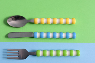children tableware ( knife, fork, spoon) set on green blue background