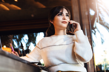 Young woman talking on cell phone while sitting alone in coffee shop.Smiling girl has telephone conversation while resting in cafe