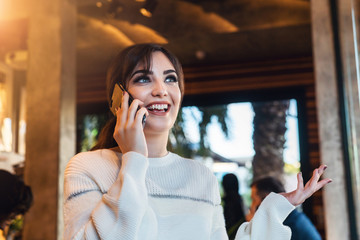 Young woman talking on cell phone while sitting alone in coffee shop.Smiling girl has telephone conversation while resting in cafe