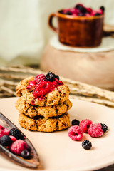 Homemade vegan crunchy oatmeal cookies with raspberry jam and date caramel on a grey wooden background.