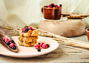 Homemade vegan crunchy oatmeal cookies with raspberry jam and date caramel on a grey wooden background.