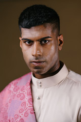 Portrait of a young and handsome Malaysian Indian Muslim man in a cream colored traditional baju melayu outfit with a striking pink sash. He is dressed festively to go visiting for Raya.