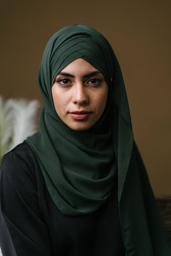 Close Up Studio Portrait Of A Beautiful, Elegant And Attractive Young Middle Eastern Muslim Woman In A Black Dress And An Olive Green Hijab Head Scarf. She Has A Neutral Expression. 