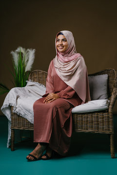 Studio portrait of a beautiful, vital and attractive young Indonesian Asian Muslim woman in a pink baju kurung dress and hijab head scarf. She is smiling naturally as she looks away from the camera.