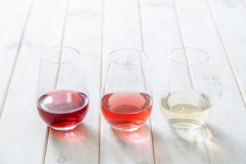 WIne tasting concept - red, rose and white wine in glasses on wood background