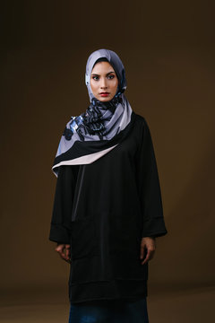 Studio portrait of a tall, slim, elegant and beautiful Middle Eastern Muslim woman in a flowing traditional black dress with a turban head scarf. She is dressed to celebrate Raya.