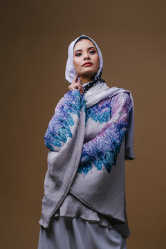Portrait of a young, elegant, tall and slim Middle Eastern Muslim woman in a flowing traditional blue dress with a hijabi turban. She is dressed to celebrate Raya.&nbsp;