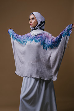 Portrait of a young, elegant, tall and slim Middle Eastern Muslim woman in a flowing traditional blue dress with a hijabi turban. She is dressed to celebrate Raya.&nbsp;