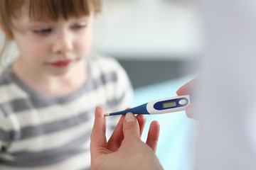 Female hand holding thermometer measuring sick little girl closeup