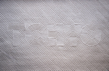 Japanese Zen garden raked with the word TOKYO in capital letters in textured white sand
