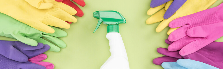 panoramic shot of bright rubber gloves in circle around spray bottle with detergent on green background