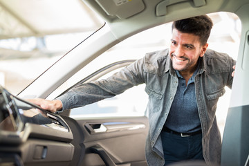 Young smiling man taking taking look to car in showroom