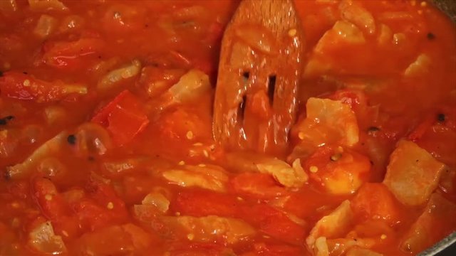 A steady, extreme close up shot of a wooden spoon stirring the cooking vegetables.