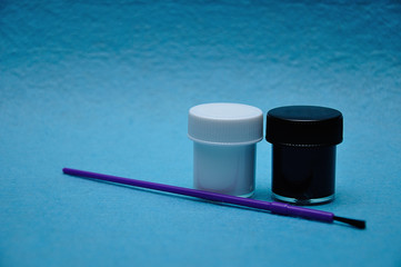 Two pots of paint with a purple paintbrush on a blue background
