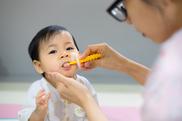 Mother is brushing her daughter teeth. Asian baby girl toothbrush by her mom. - 268785677