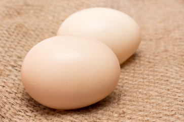 Two chicken eggs on a rough brown sack_