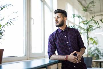 Cheerful indian business man standing near the window in modern office
