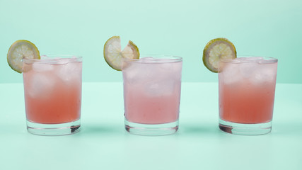 Glass of cocktail drink with lemon slice and ice cubes against mint background