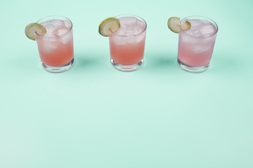 Three glasses of grapefruit juice with lemon slices and ice cubes over the mint background