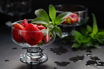 Fresh ripe red strawberries in a glass bowl on a black background