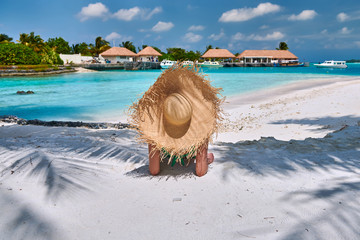 Fototapeta na wymiar Woman sitting on beach under palm tree
