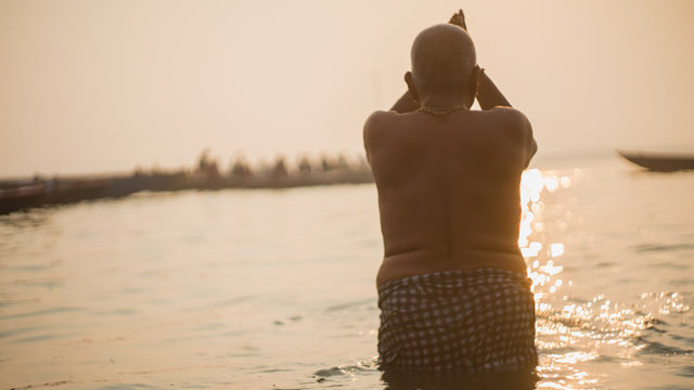 Old Hindu Man Praying And Bathing In Ganges River During Sunrise In Varanasi, India