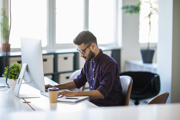 Fototapeta premium Handsome young indian business man with working place in creative office