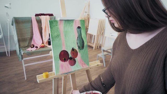 Female young artist paints still life