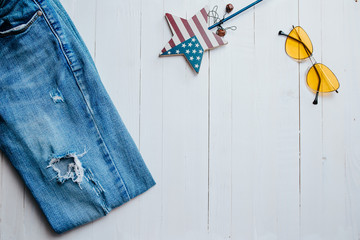 Blue ripped jeans, sunglasses and american star on the white wooden background.