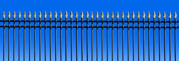 Fence in wrought iron with golden spears on blue sky background