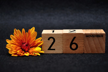 26 November on wooden blocks with am orange daisy on a black background