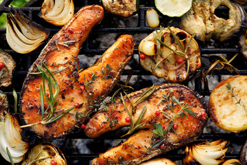 Grilled salmon steak with the addition of rosemary, aromatic spices and vegetables on the grill plate outdoors, close-up view