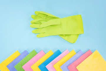 top view of green rubber gloves and multicolored rags on blue background