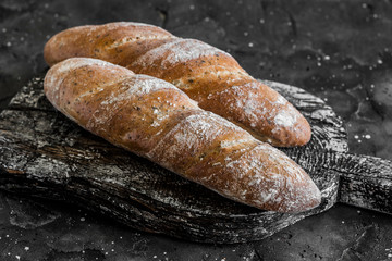 Homemade whole-grain baguettes with provencal herbs on rustic wooden board, on a dark background