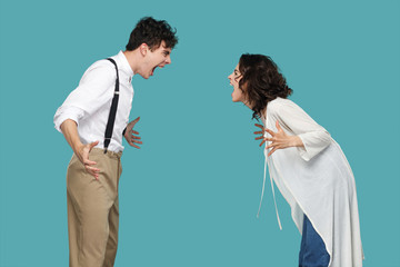 Profile side view portrait of two aggressive brunette partner standing and screaming at each other. conflict between to friend, partners or family. indoor studio shot isolated on blue background.