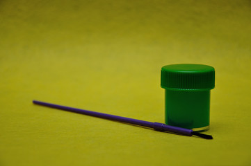 Fototapeta premium A pot of green paint with a purple paintbrush on a yellow background