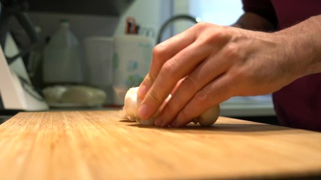 Person cutting mushrooms on a wooden board in the kitchen at home. Image of hands, mushrooms cut and bottom part of the kitchen