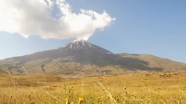 A great shot of Damavand snowy peak and foothill and clouds moving over 3 A 4K shot of Damavand's snowy peak and some clouds moving over in blue sky and yellow plants shaking by wind landscape