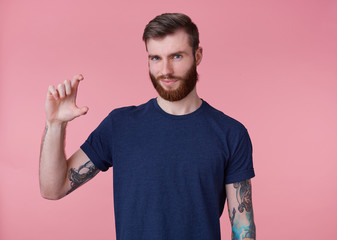 Portrait of young attractive red-bearded guy, frowning and looking at the camera, shows fingers...