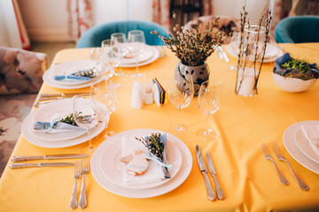 table setting. The dining table is covered with a yellow tablecloth. White plate on a yellow tablecloth. Glass wine glasses on the table.