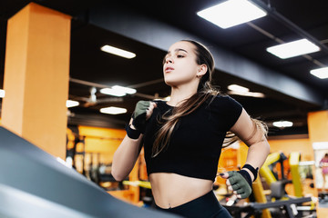 Fototapeta na wymiar Portrait of a serious hardy young female running on a treadmill after a strength training in the hall. Concept of goal and fit shape without fat