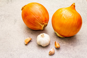 Giant onion bulbs with garlic for scale on a stone background. Food cooking background, close up.
