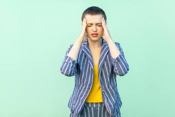 Headache or confusion. Portrait of handsome beautiful short hair young woman in casual striped suit standing holding her painful head or thinking. studio shot isolated on light green background.